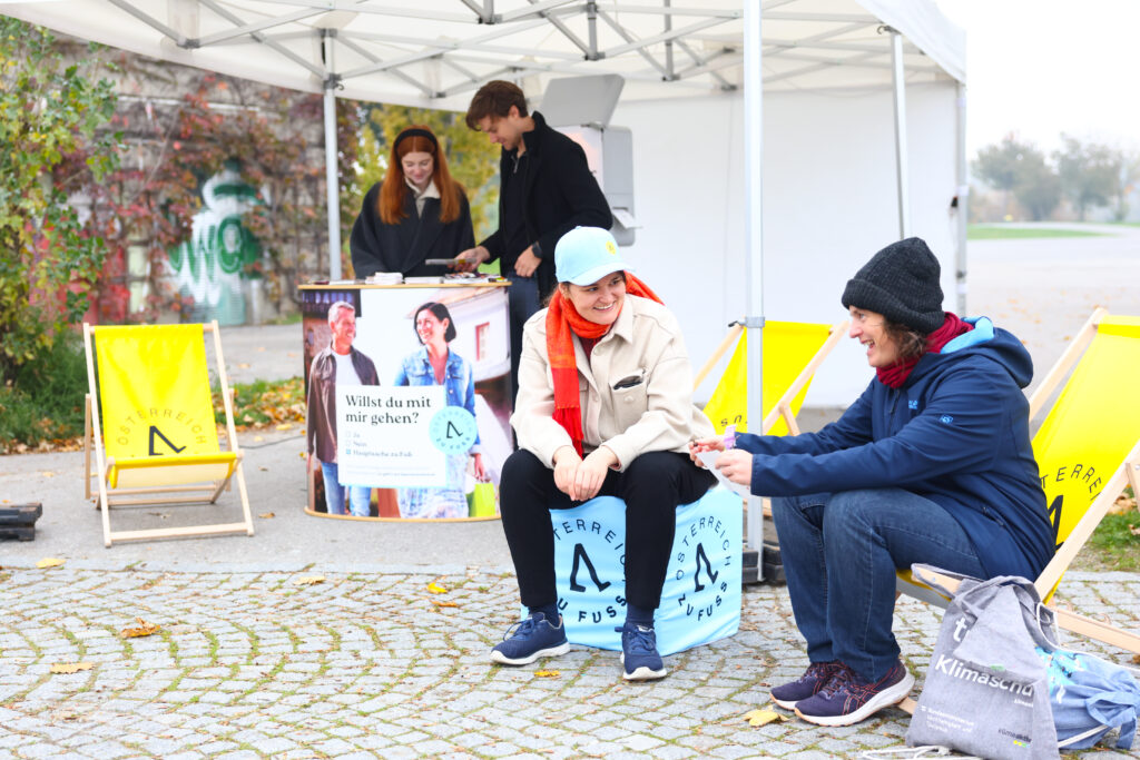 Zwei Personen sitzen vor dem Stand von "Österreich zu Fuß" bei 12h LiDo